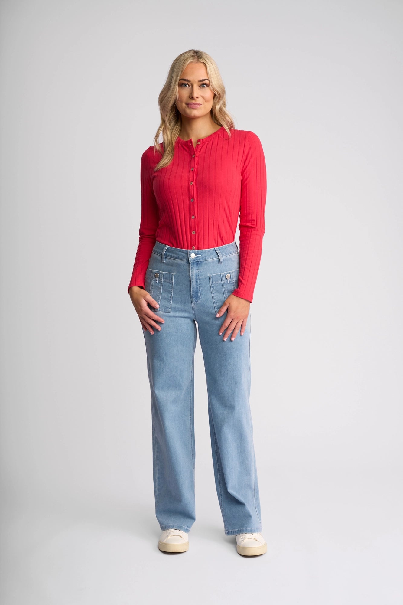 A person stands facing forward against a plain light background, wearing white sneakers, a long-sleeve red shirt, and the Vassalli Lottie Jean in Light Wash Denim.