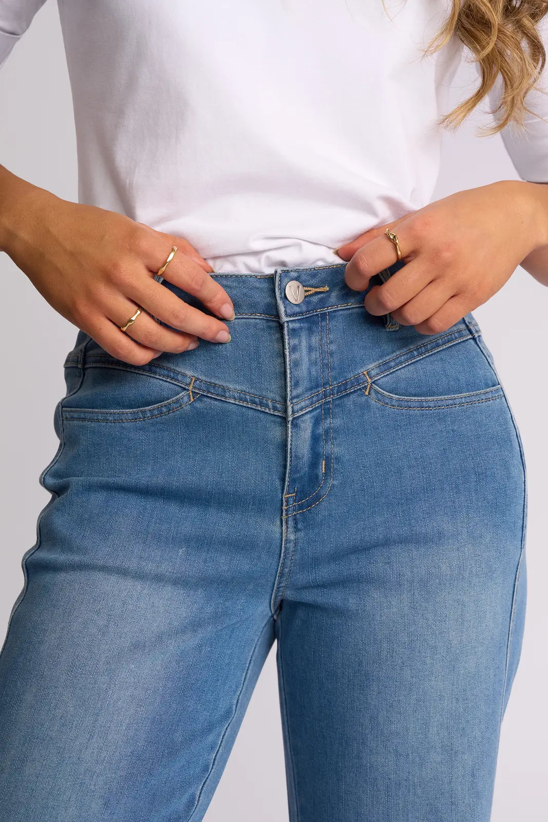 A person wearing a white shirt and the Vassalli Apollo Jean in Vintage Denim stands with hands at the waistband, displaying gold rings on both hands. The image is cropped from the chest to mid-thigh.