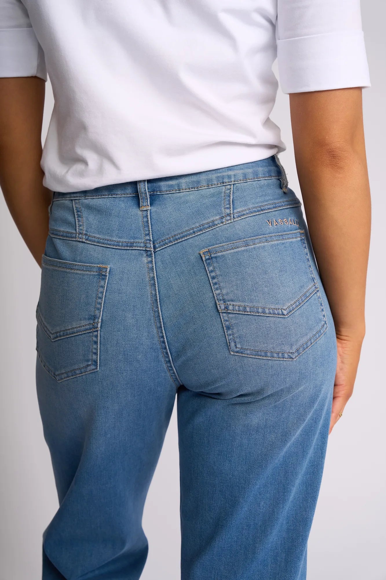 A person is shown from the back wearing Vassalli’s Apollo Jean - Vintage Denim, a light blue barrel-leg style featuring two back pockets, paired with a white short-sleeve shirt and their right hand relaxed by their side.