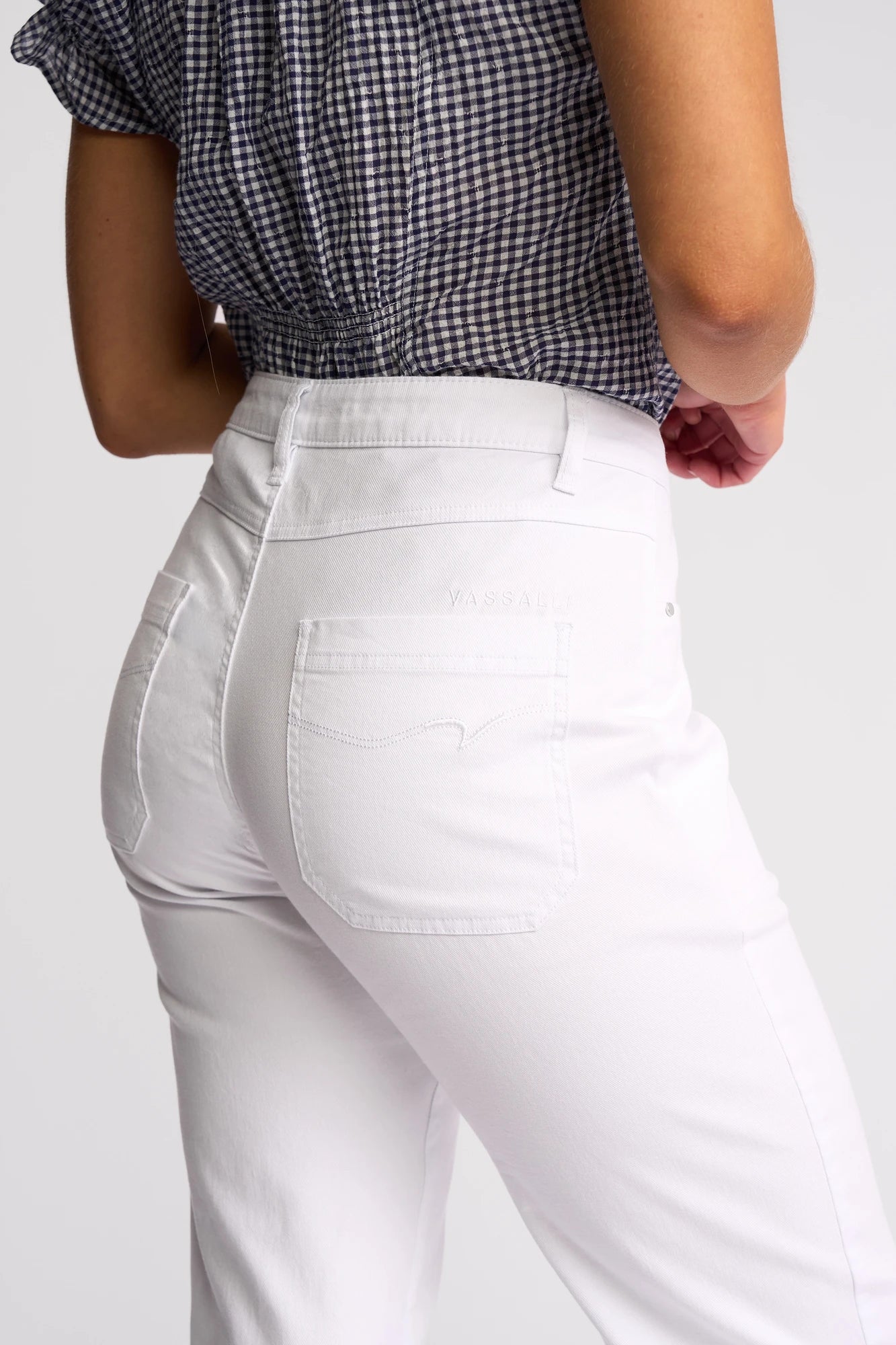 A person shown from the back and waist down is wearing the Vassalli Villa Jean in white denim, paired with a black-and-white checkered top, standing against a plain background.