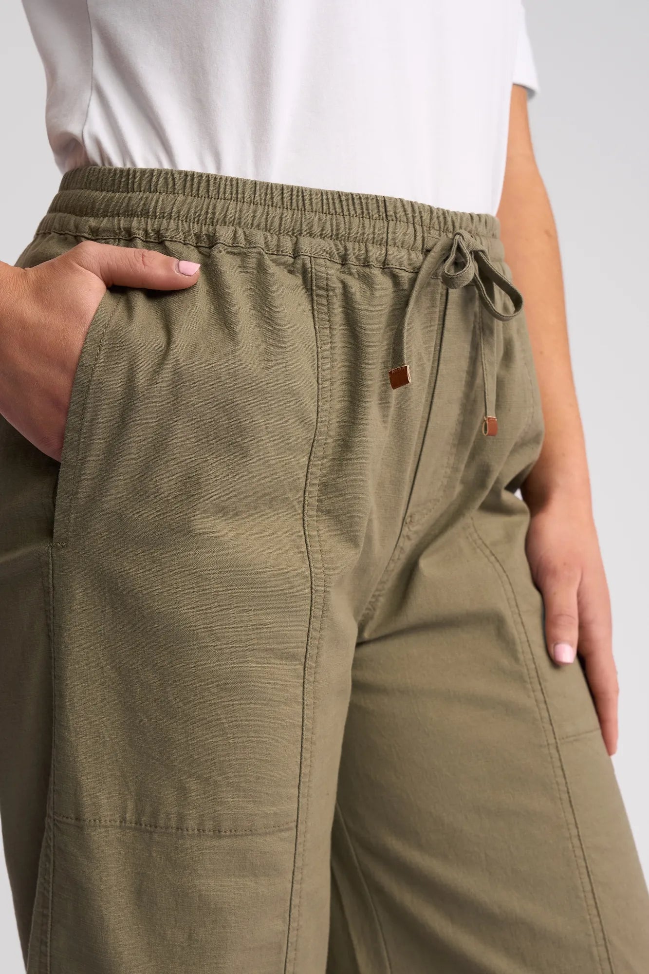 A person wearing the Vassalli Dione Pant in Army and a white shirt has one hand in a pocket and the other resting by their side. The image displays only the waist and upper legs.