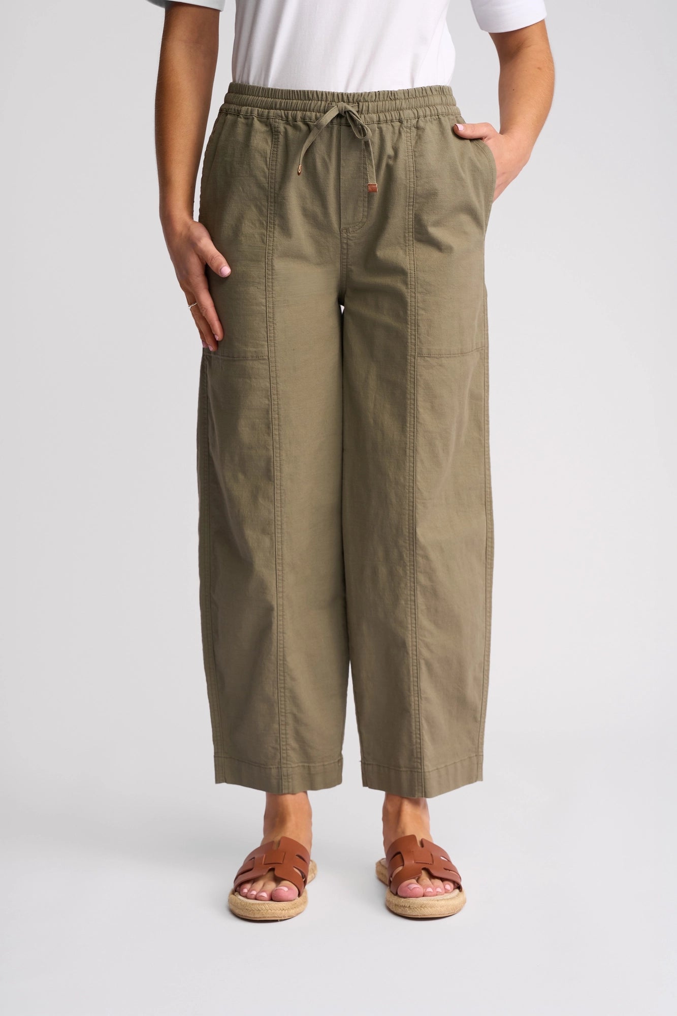 A person wearing the Vassalli Dione Pant - Army, styled with a white shirt and brown sandals, stands against a plain light background. Only the lower half of the body is visible.