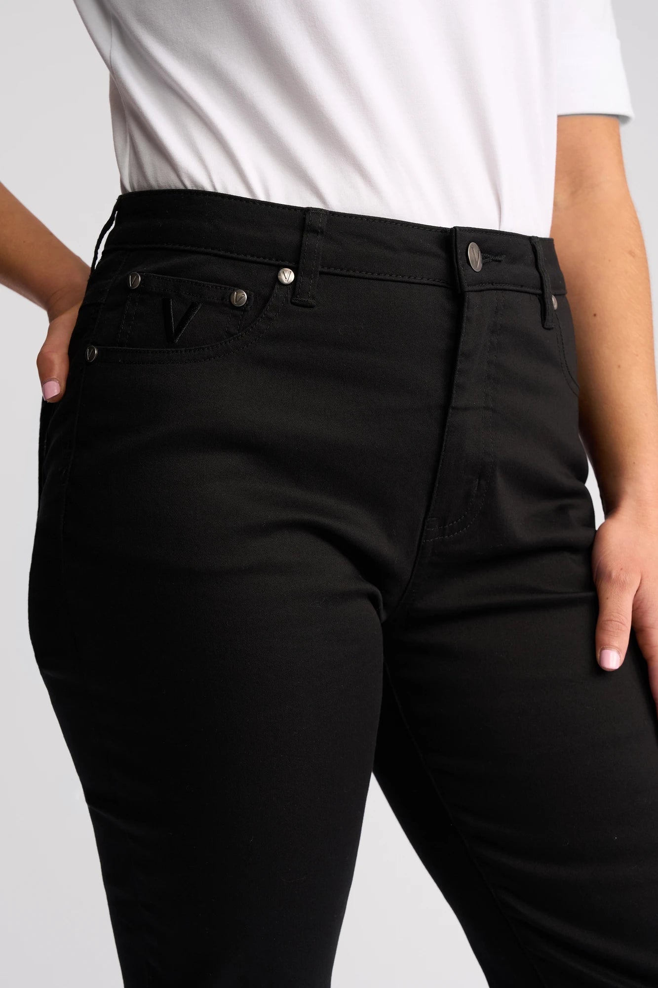 Wearing a white shirt and the Vassalli Arrival Pant - Black, a person stands with one hand on their hip, highlighting the front and side details of these slim-leg pants made from stretch cotton.