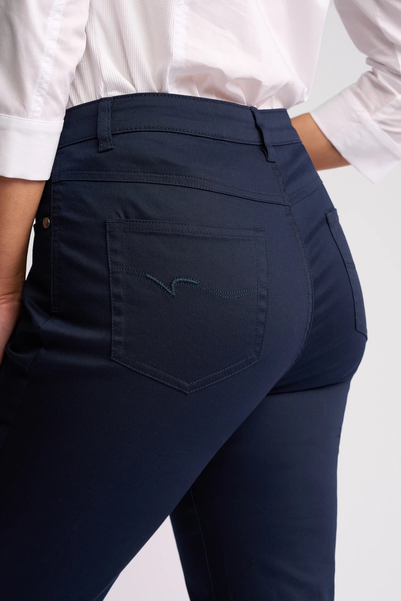 A person is shown from the waist down wearing Vassalli’s Arrival Pant in Navy, featuring a slim-leg design in stretch cotton, paired with a white shirt. The focus is on the back pocket and hip area of the pant.