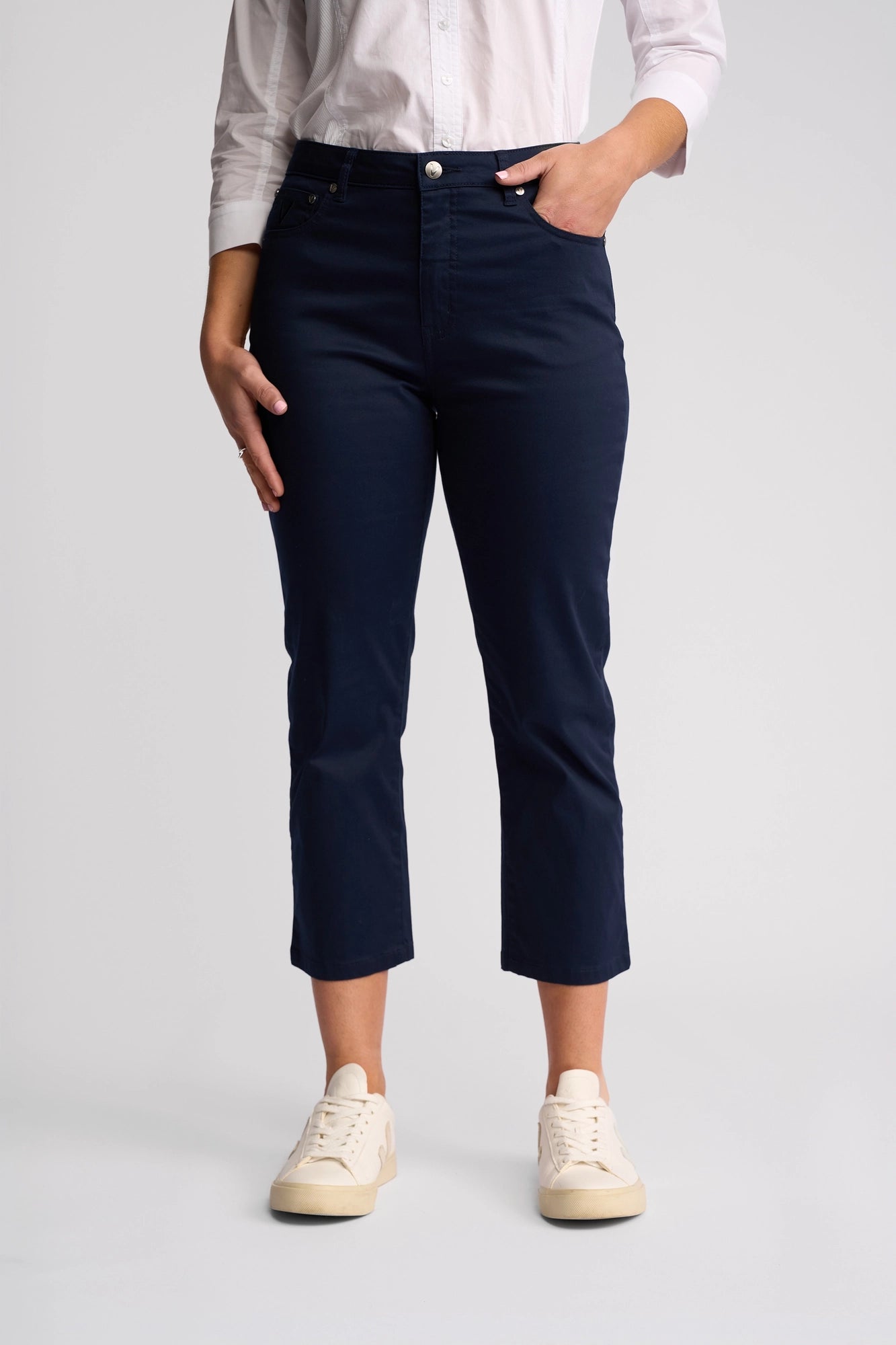 A person wearing a white button-up shirt, Vassalli’s Arrival Pant in Navy, and white sneakers stands against a plain light background with hands relaxed at their sides.