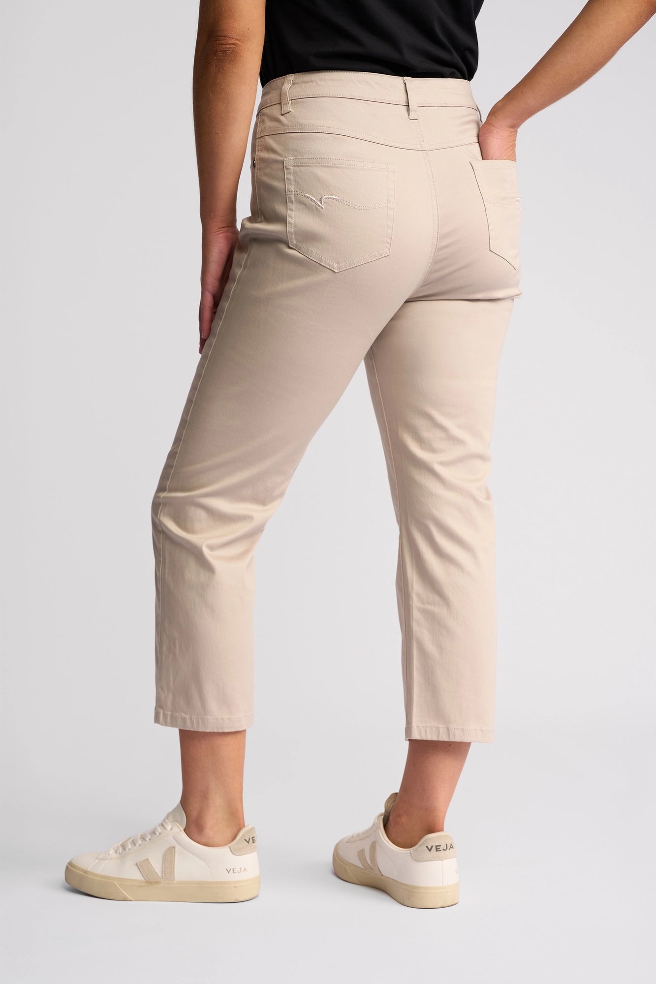 Wearing the Vassalli Arrival Pant in Pumice—a slim-leg style crafted from comfortable stretch cotton—paired with a black shirt and cream Veja sneakers, this person stands against a plain light background with their back to the camera.