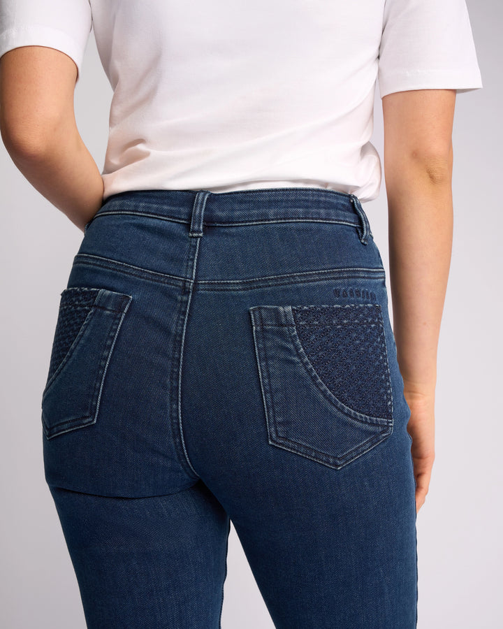 A person facing away from the camera wears a white short-sleeve shirt and Vassalli Reign Jean - Brushed Indigo, high-waisted blue skinny jeans with textured back pocket detailing.