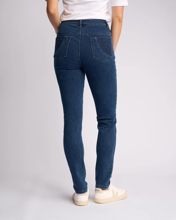 A person wearing Vassalli’s Reign Jean in Brushed Indigo stands facing away from the camera, paired with a white T-shirt and sneakers against a light background—ideal for women’s denim NZ style.