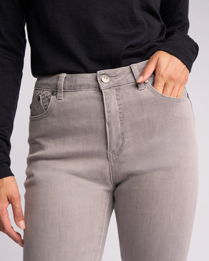 A person wears Vassalli Reign Jean - Light Grey, a high-waisted skinny-leg women’s denim, paired with a black long-sleeve shirt and one hand in the front pocket.