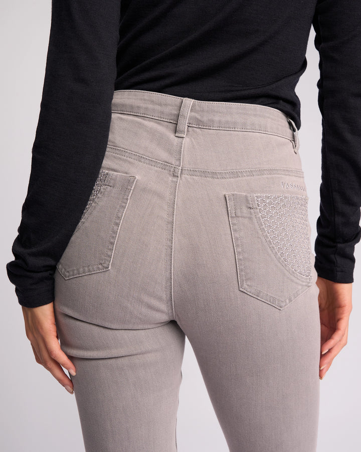 A person wearing Vassalli Reign Jean - Light Grey, featuring skinny legs and decorative back pocket stitching, paired with a black long-sleeve top; shown waist down from behind.