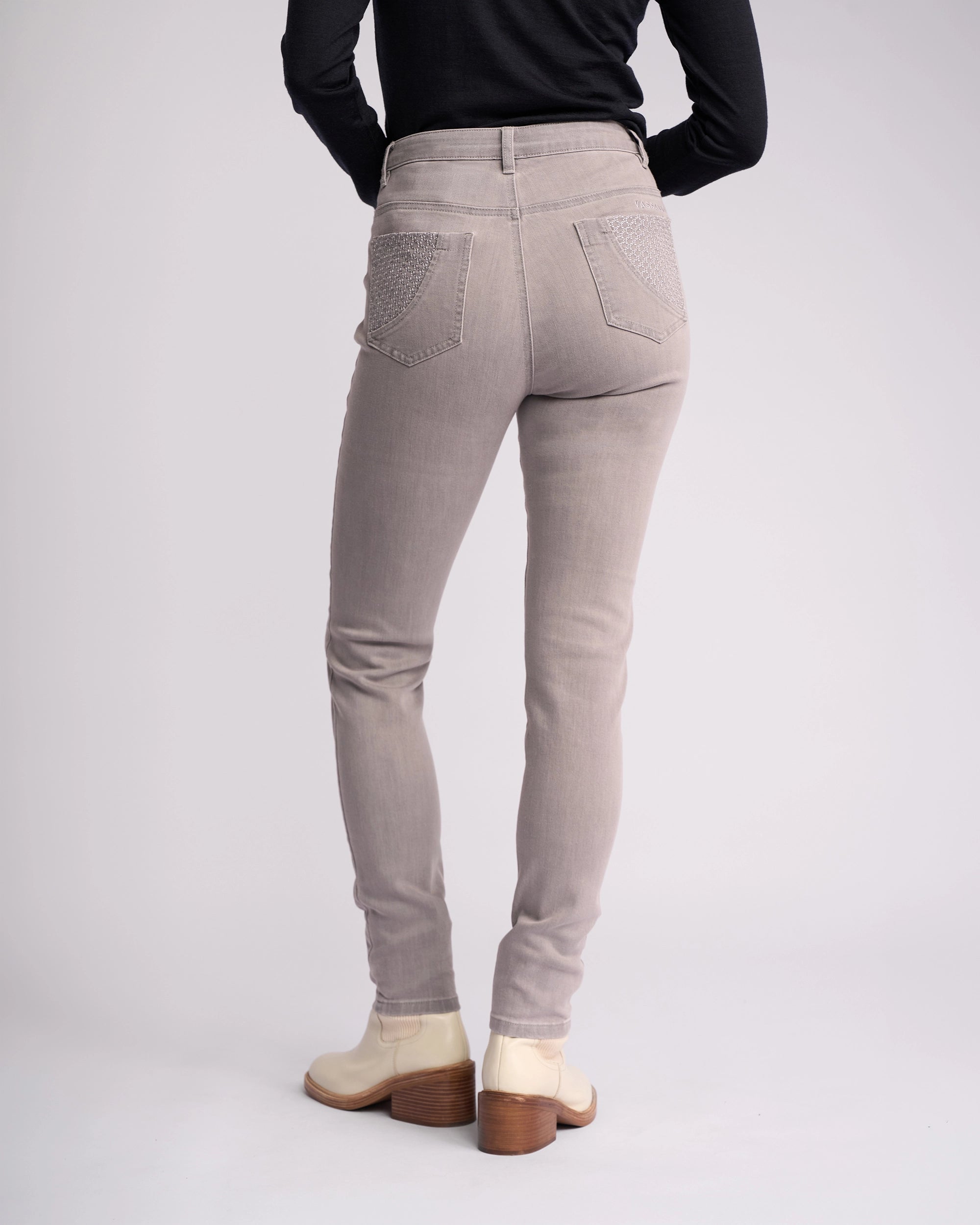 A person stands facing away from the camera in Vassalli's Reign Jean - Light Grey, paired with a black long-sleeve top and cream ankle boots against a plain light background—perfect for elevating your women’s denim NZ style.