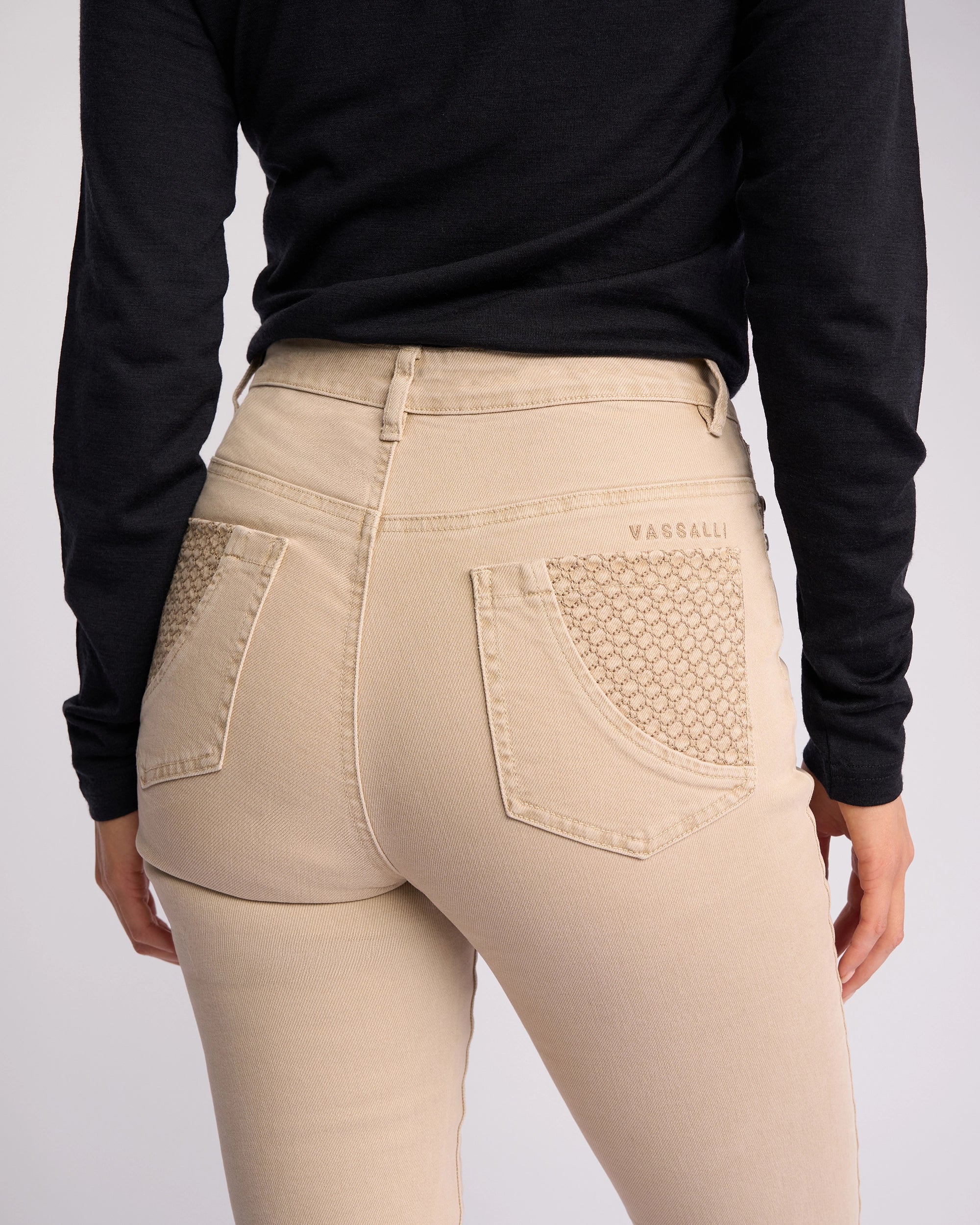 A person shown from behind, waist down, wears Vassalli Reign Jean - Oat Denim with textured back pockets and a black long-sleeve top. The Vassalli brand name appears above the right pocket.