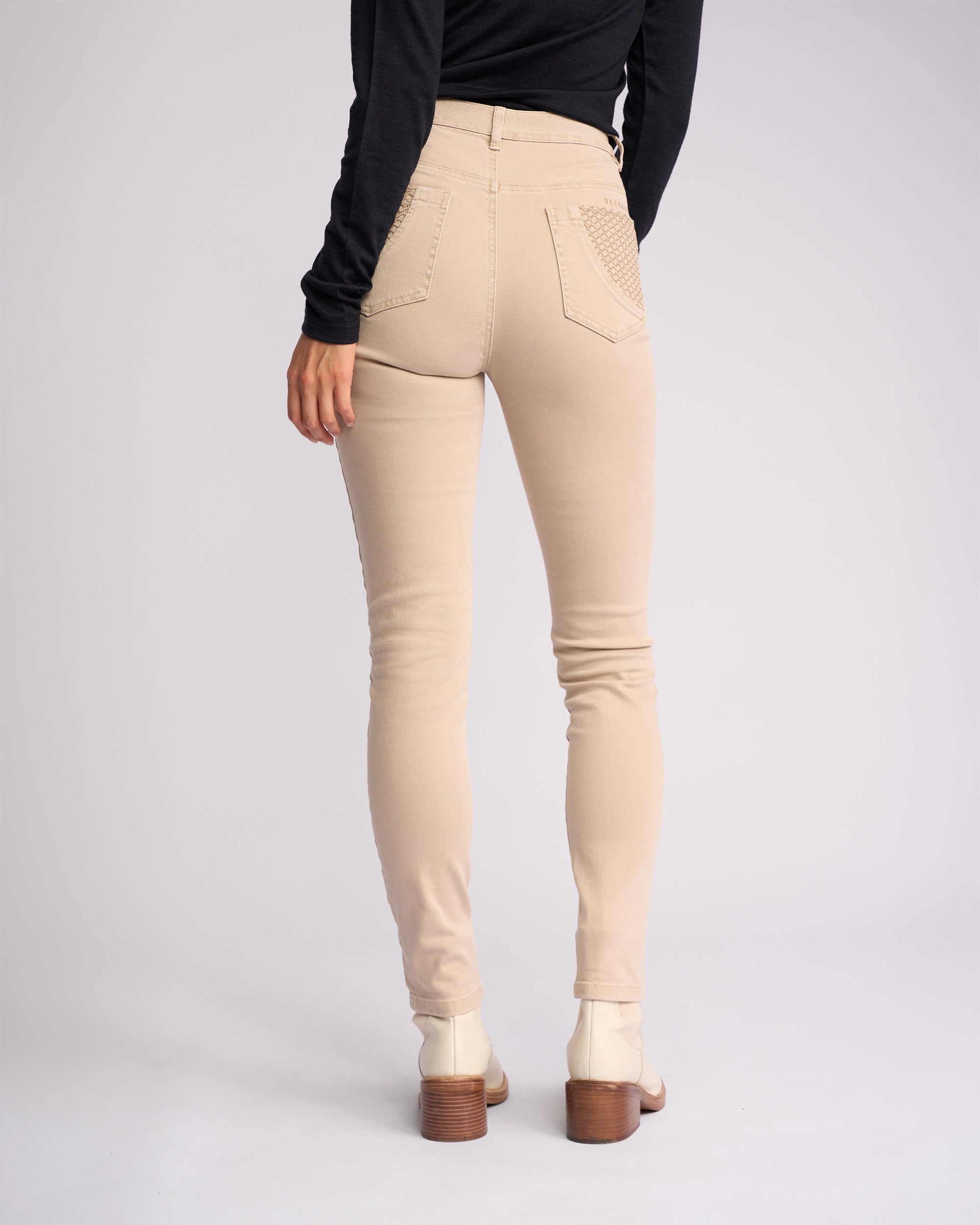 A person in Vassalli’s Reign Jean - Oat Denim, a black long-sleeve top, and white boots stands facing away, showcasing the back of the outfit against a plain light background—ideal for women's denim NZ style.
