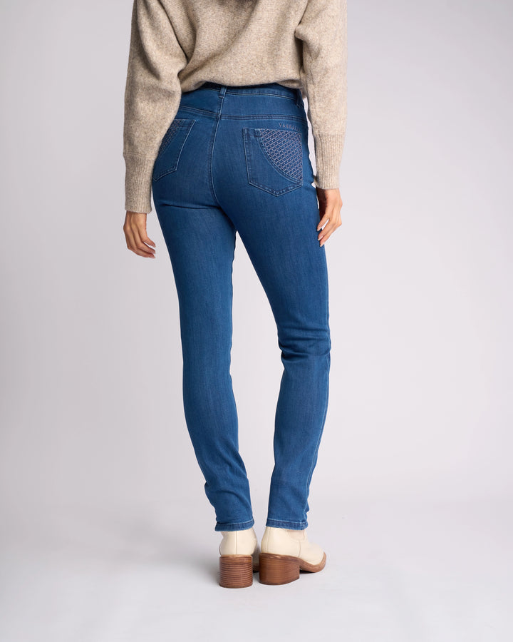 A person is shown from the back wearing a beige sweater, Vassalli Reign Jean - Plain New Blue, and light-colored ankle boots with wooden heels, standing against a plain light background.
