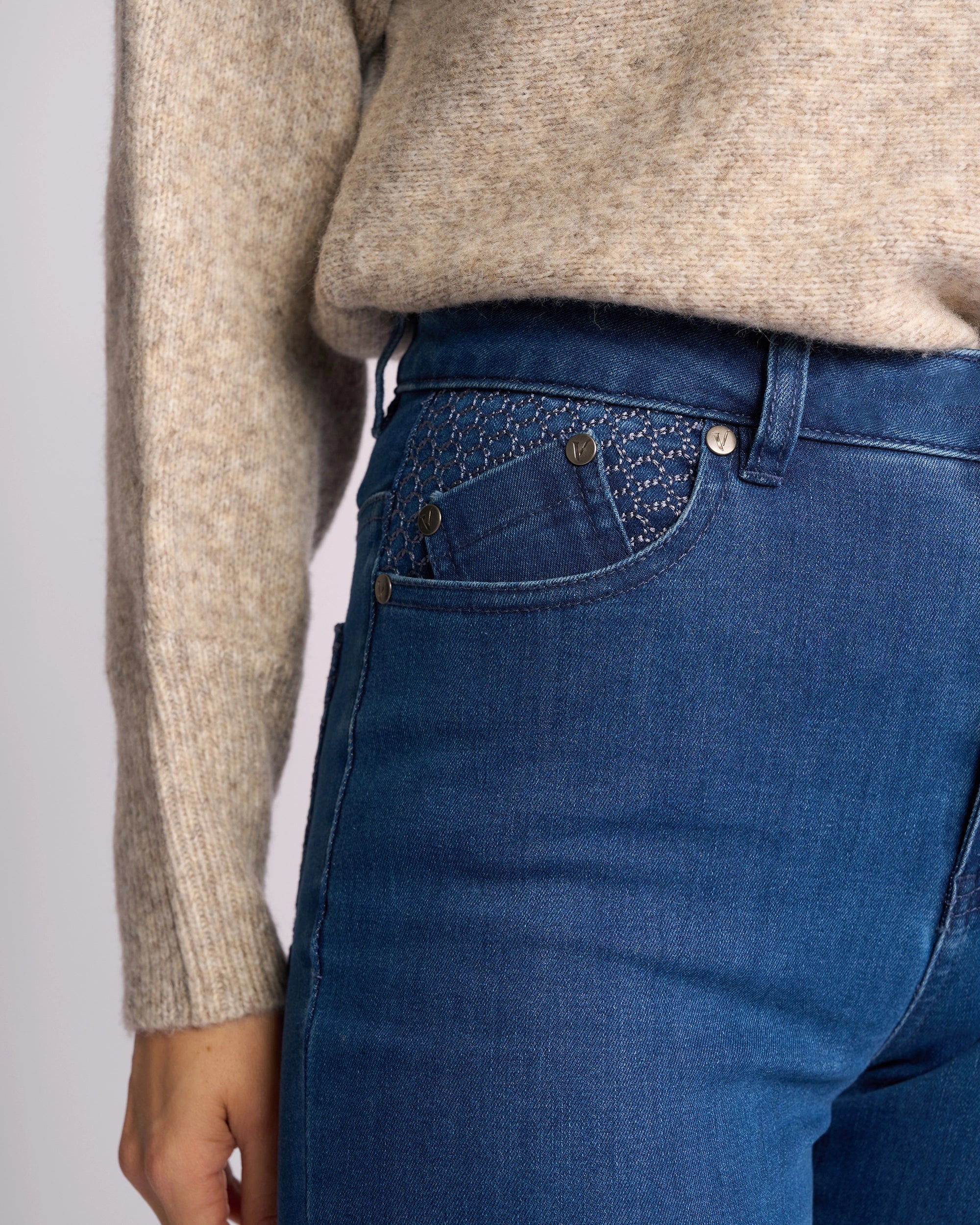 A person wears a beige knit sweater and Vassalli Reign Jean - Plain New Blue, showing only the lower torso and left arm. The high-waisted skinny-leg jeans highlight stylish women’s denim fashion from NZ brand Vassalli.