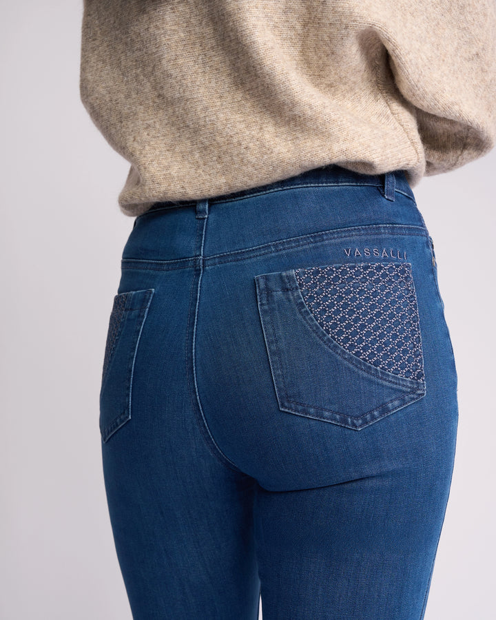 A person wears Vassalli’s Reign Jean - Plain New Blue skinny-leg women’s denim with plain back pockets, paired with a beige knit sweater. "Vassalli" is embroidered above the right pocket; shown from the waist down and back.