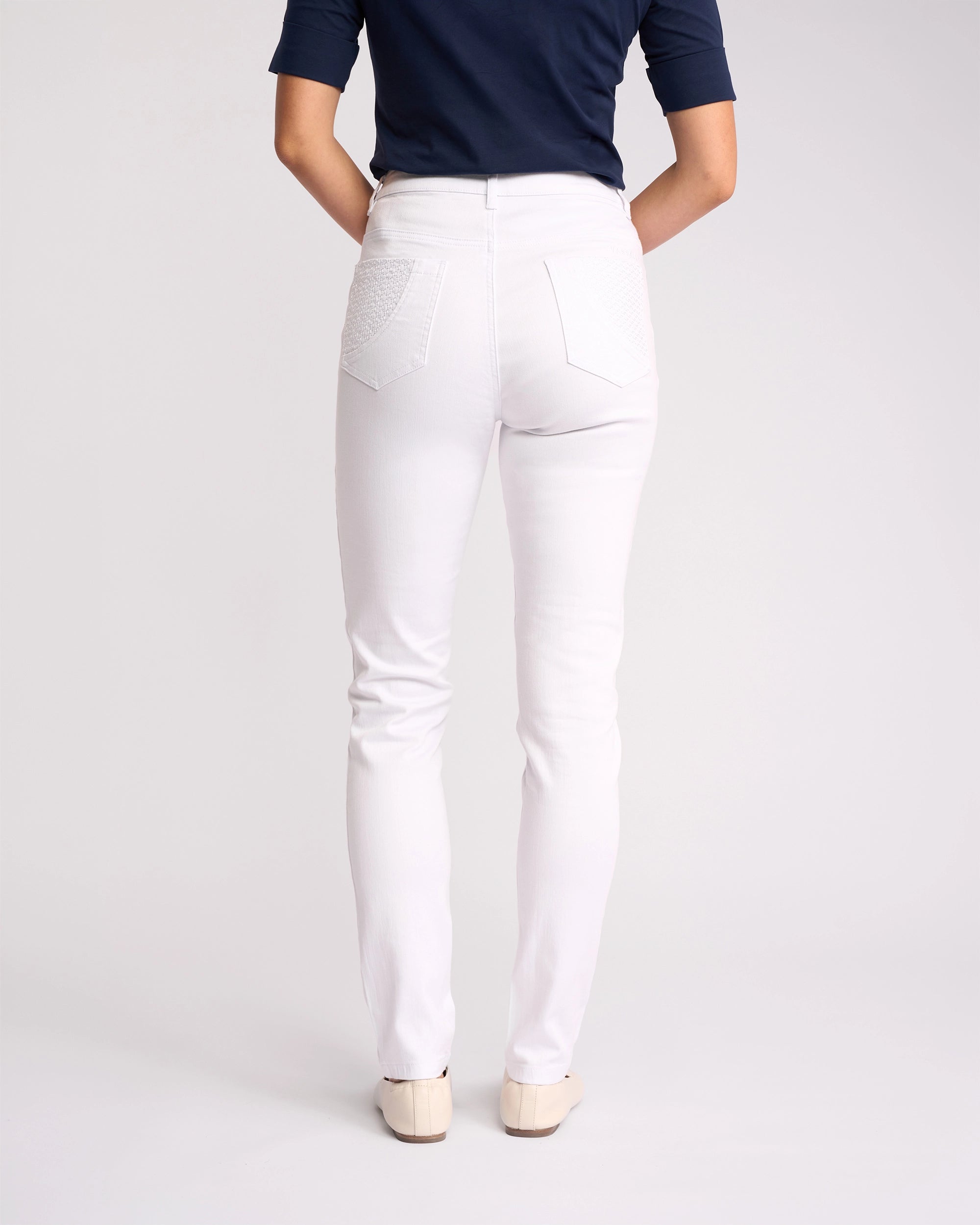 A person faces away, wearing a navy short-sleeve shirt and Vassalli Reign Jean - White Denim, paired with cream shoes against a plain background—a flawless nod to women’s denim NZ style.