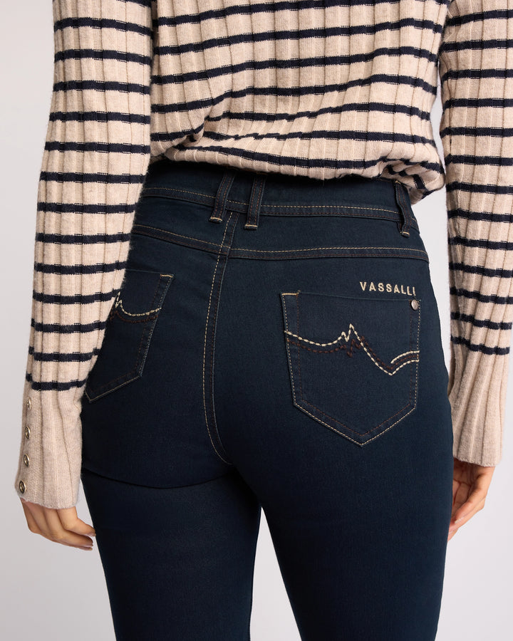 Wearing Vassalli’s Pace Jean in Indigo Denim, featuring stretch fabric and back pocket embroidery, paired with a beige striped long-sleeve sweater. The image highlights the lower back and waist.
