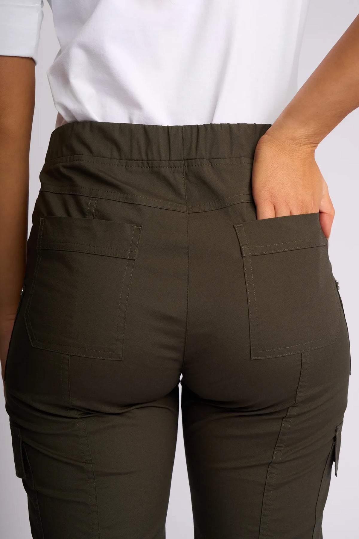 A person wearing the Vassalli Wave Pant in Khaki, crafted from stretch cotton, and a white shirt is shown from the back with one hand placed inside the right back pocket of the pants.