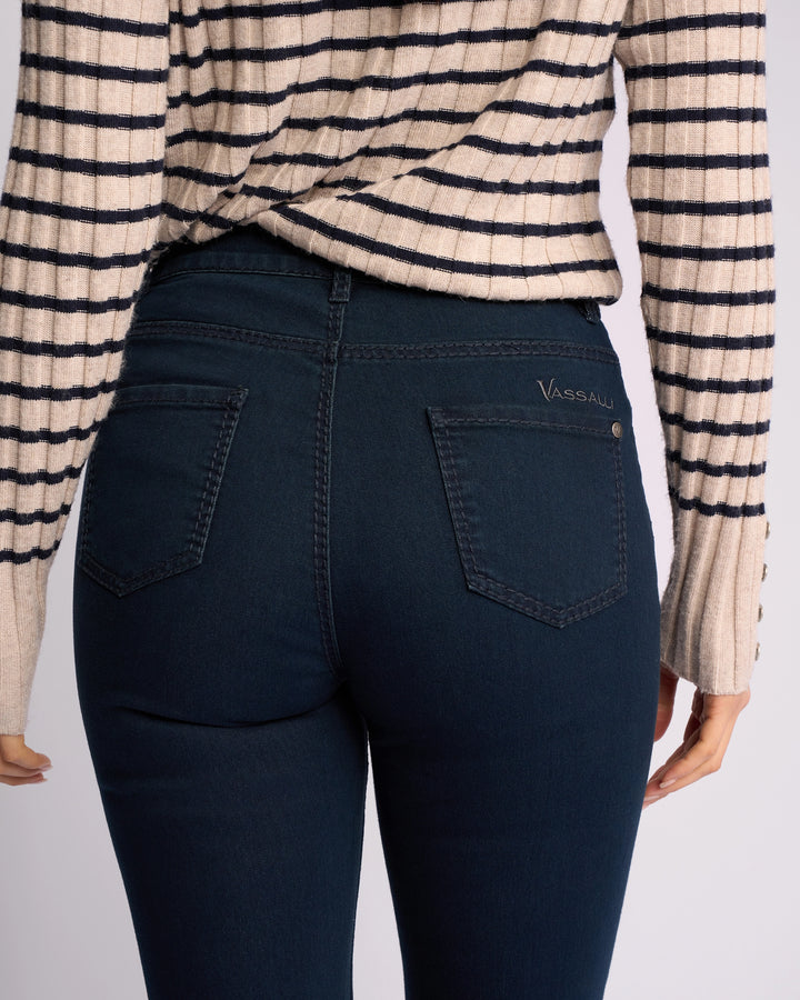 A person is shown from the back wearing a cream and black striped sweater and dark blue Vassalli Lotus Jean - Indigo Denim, crafted from stretch denim with two back pockets and a small logo on the right pocket.