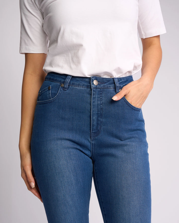 Model wears a white short-sleeve shirt paired with Vassalli's Icon Jean - Blue Denim, shown from shoulders to mid-thigh with one hand in a pocket against a plain background.