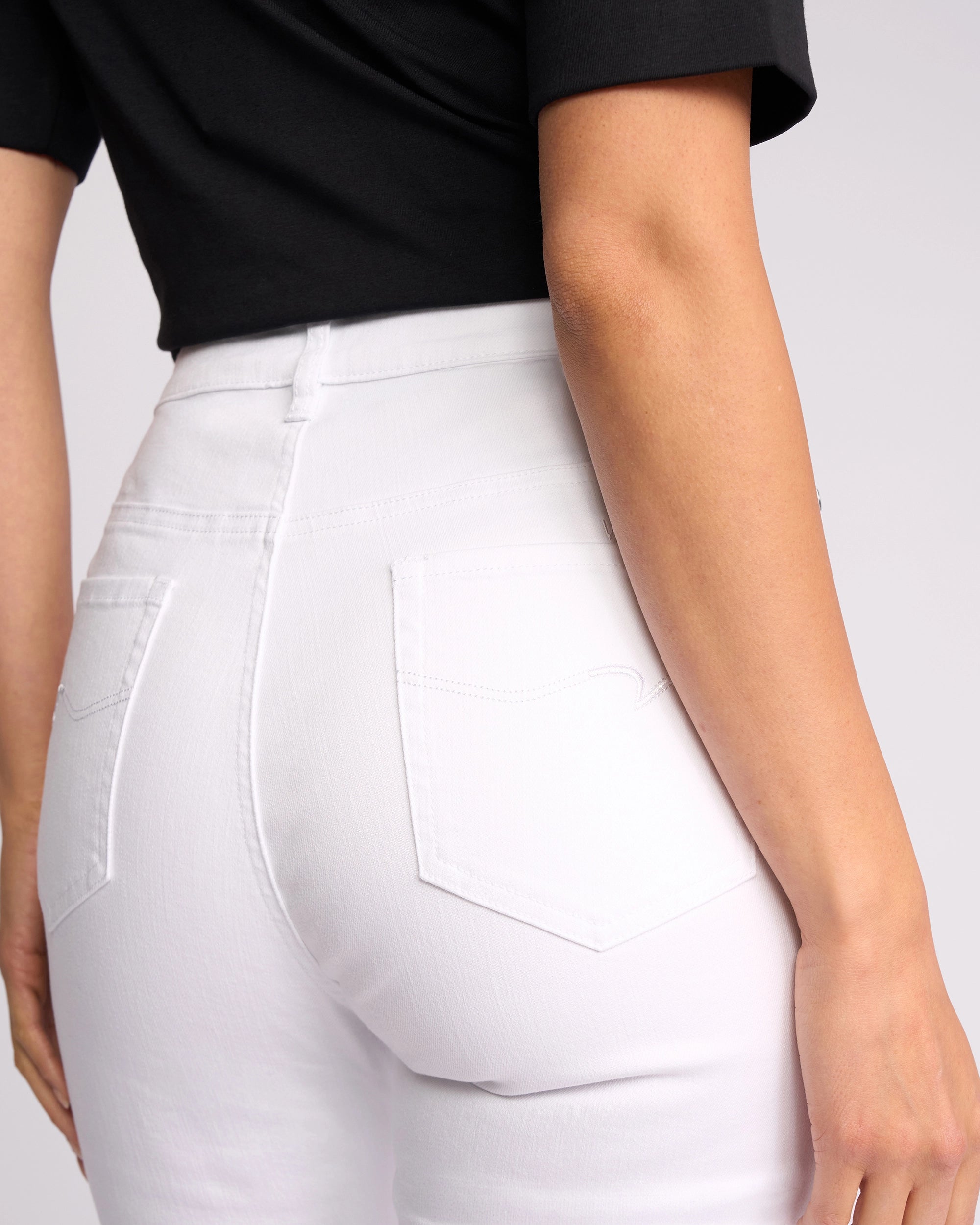 A person wearing Vassalli’s Icon Jean in White Denim, shown from the back and waist down, highlights the flattering fit, ankle-grazer length, and back pockets of these high-waisted skinny jeans.