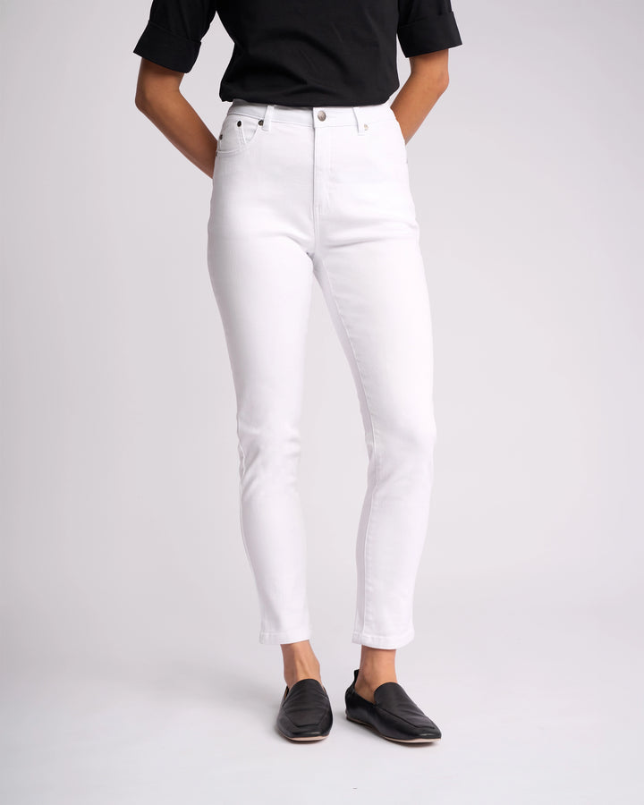 Person wearing a black short-sleeve top, Vassalli Icon Jean - White Denim (high-waisted, skinny-leg), and black slip-on shoes, standing against a plain light background. The person's face is not visible.