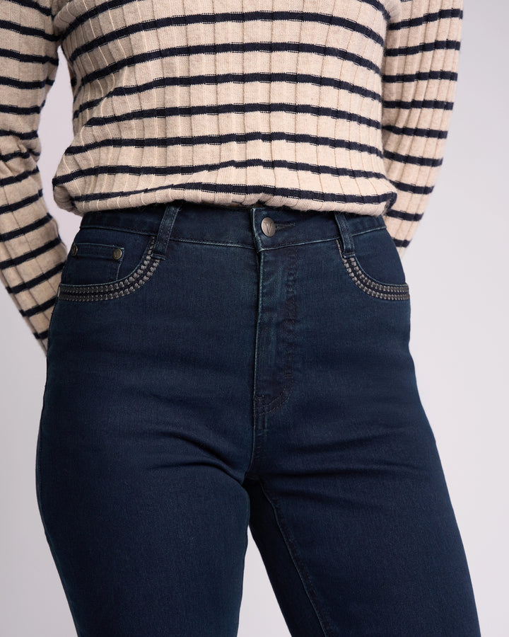 A person models the Vassalli Urban Jean - Mid Blue, styled with a beige sweater featuring black horizontal stripes, tucked in and shown from shoulders to mid-thigh against a plain background.