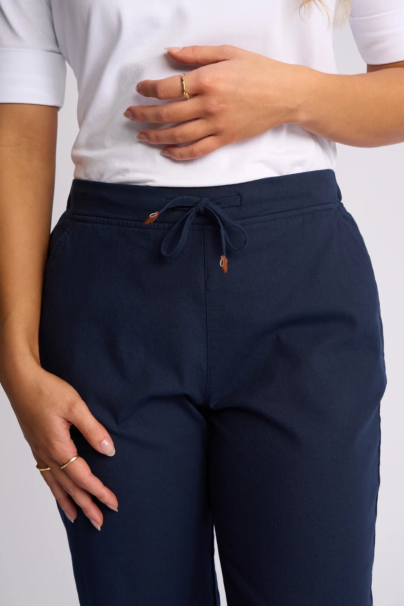 A person wearing a white shirt and Vassalli Drew 3/4 Pant in Ink stands with one hand on their waist and the other resting on their thigh, displaying several rings.