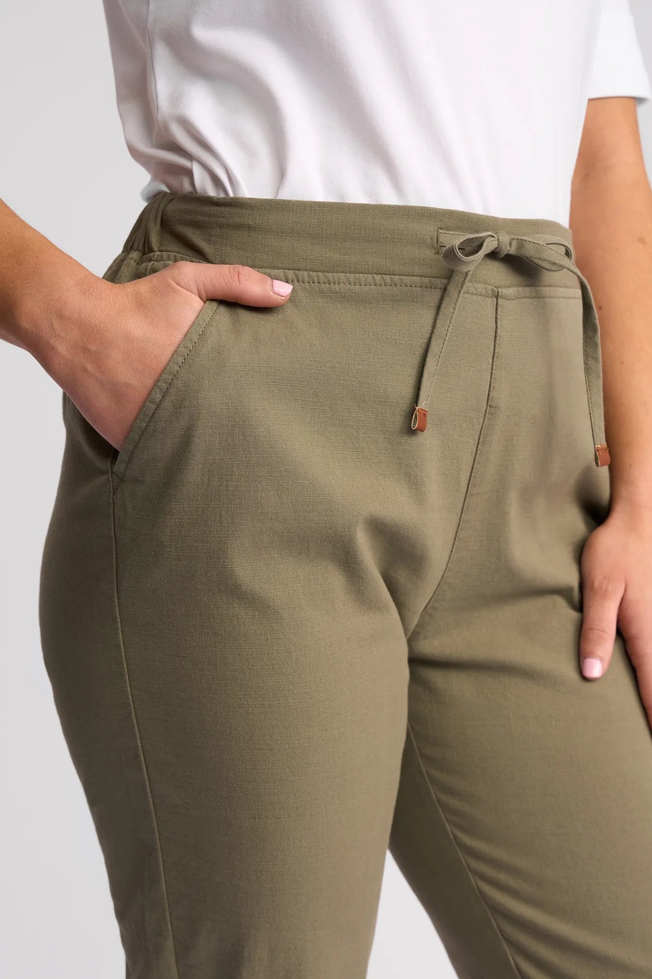 A person wearing Vassalli Denver 7/8 Pant - Army stretch cotton drawstring pants, with one hand in the pocket, stands against a plain background. The person is also wearing a white shirt.