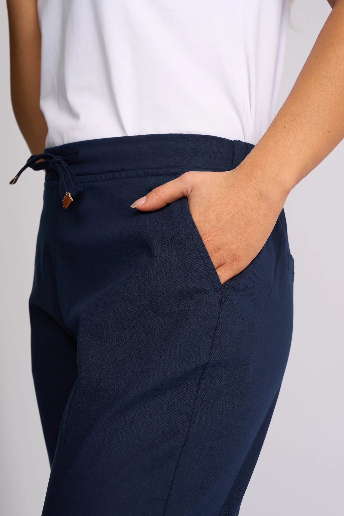 A person wearing a white shirt and Vassalli Denver 7/8 Pant in Ink stands with one hand in their pocket, facing slightly sideways.