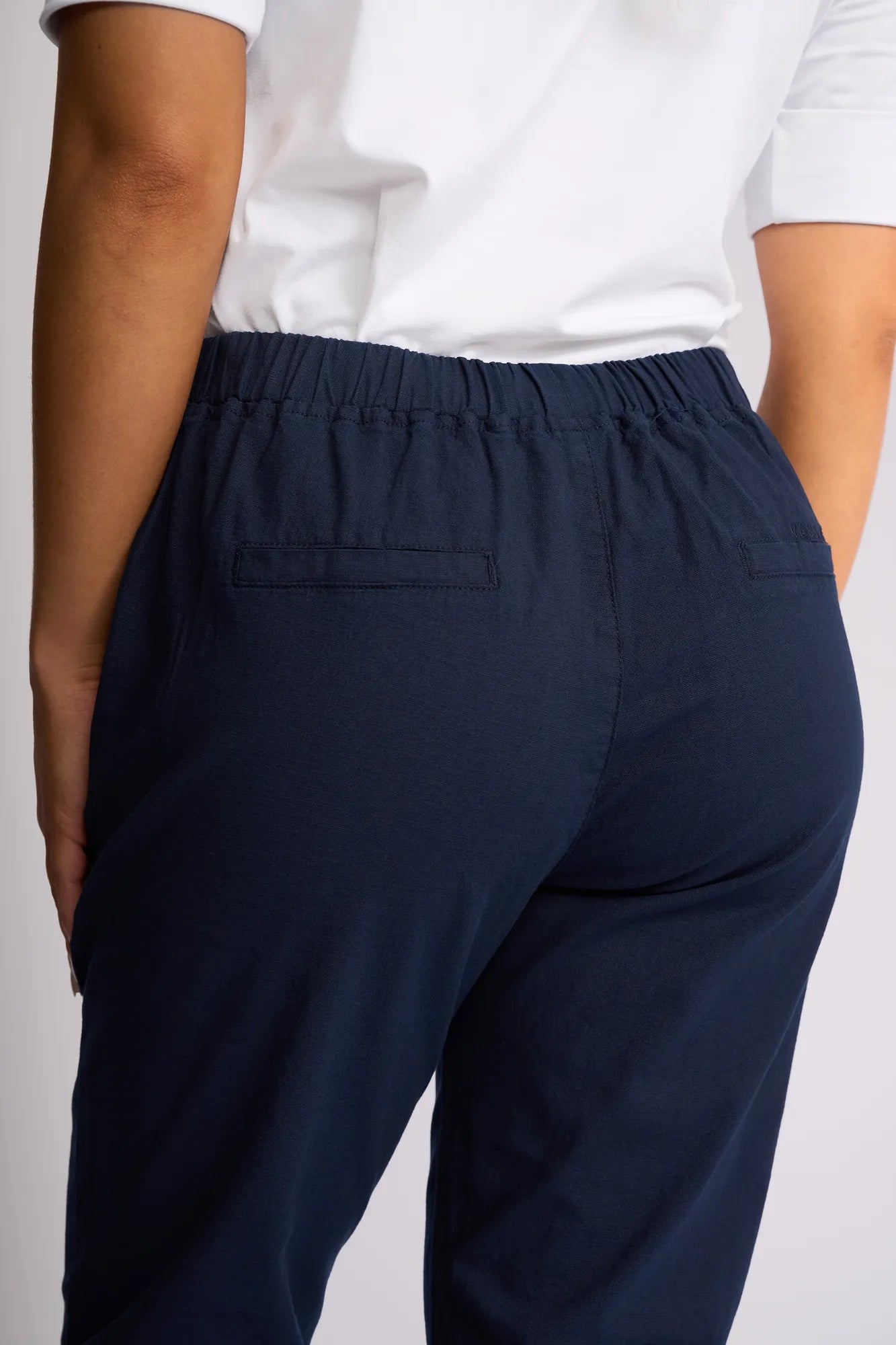 Someone wearing a white shirt and Vassalli’s Denver 7/8 Pant - Ink—crafted from stretch cotton in a skinny-leg style—is pictured from the back, one hand resting at their side.