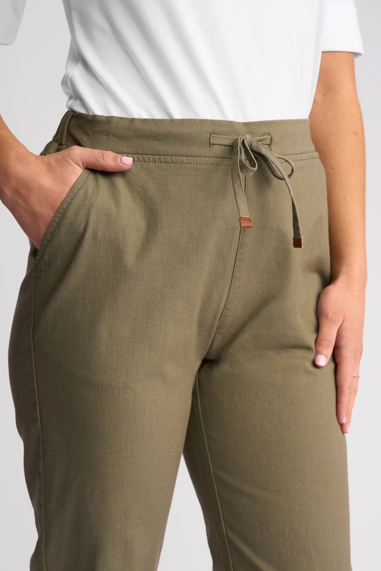 A person wearing the Vassalli Henley 7/8 Pant in Army, made from stretch cotton, with one hand in their pocket, paired with a white shirt.
