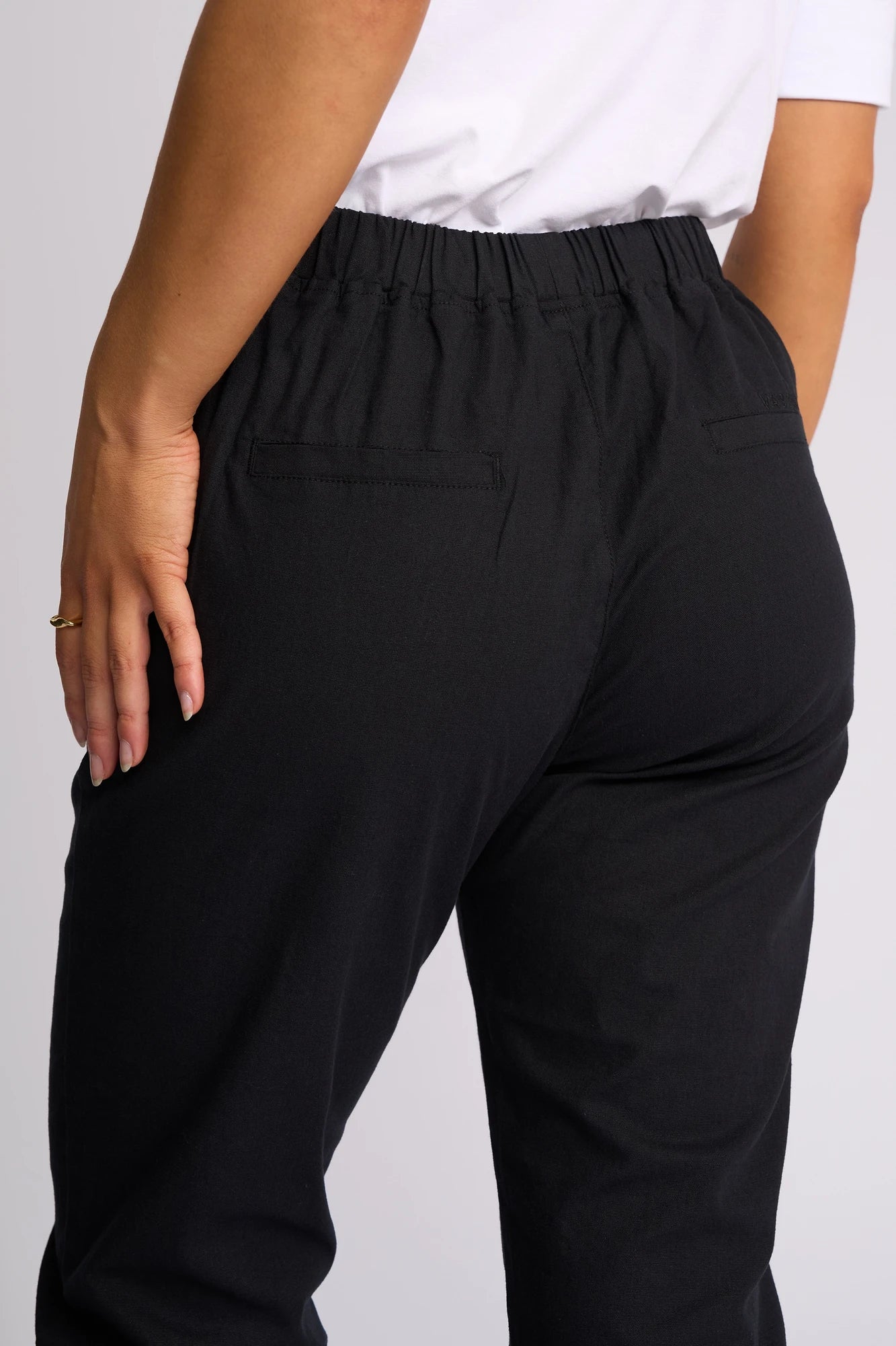A person is shown from the back wearing Vassalli’s Henley 7/8 Pant in black and a white shirt, with one hand resting on their hip.