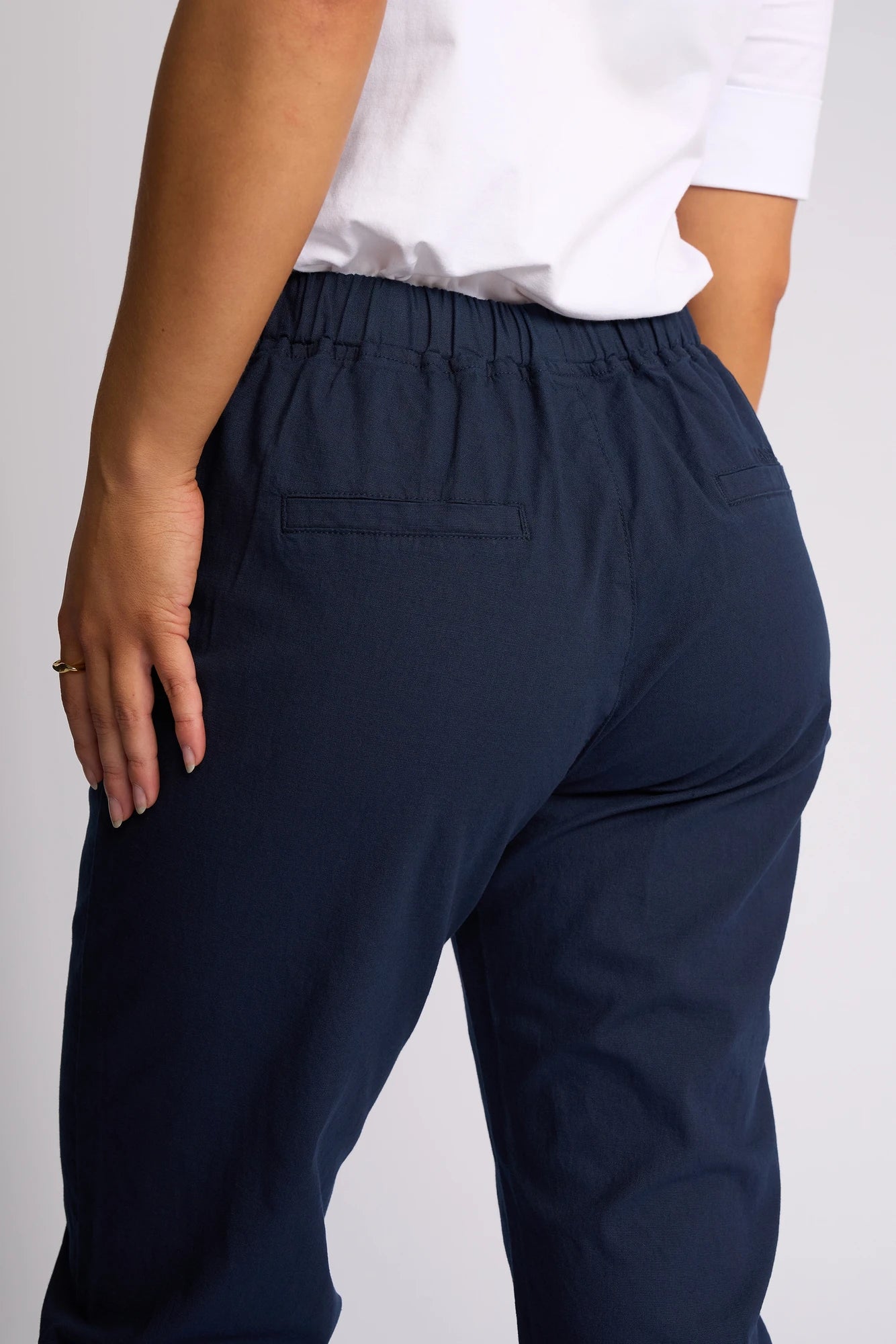 A person wearing a white shirt and Vassalli Henley 7/8 Pant in Ink, shown from the back with one hand resting on their hip.