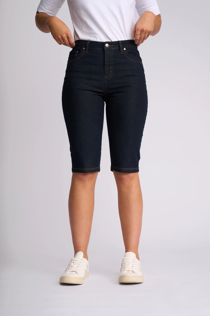 A person is wearing the Vassalli Alfa Short - Indigo Denim (Contrast Stitch) paired with a white shirt and white sneakers, standing against a plain light background. Their hands are near their waist, and their face is not visible.