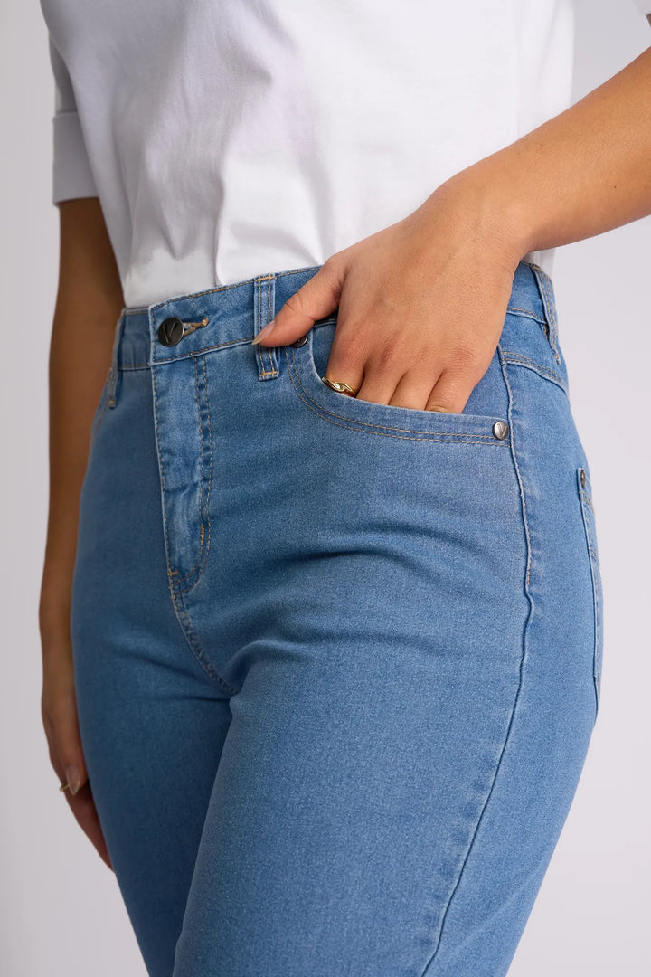 A person wearing the Vassalli Alfa Short - Light Denim (Contrast Stitch), crafted from lightweight stretch denim, and a crisp white shirt stands with one hand in their front pocket—a true summer staple.