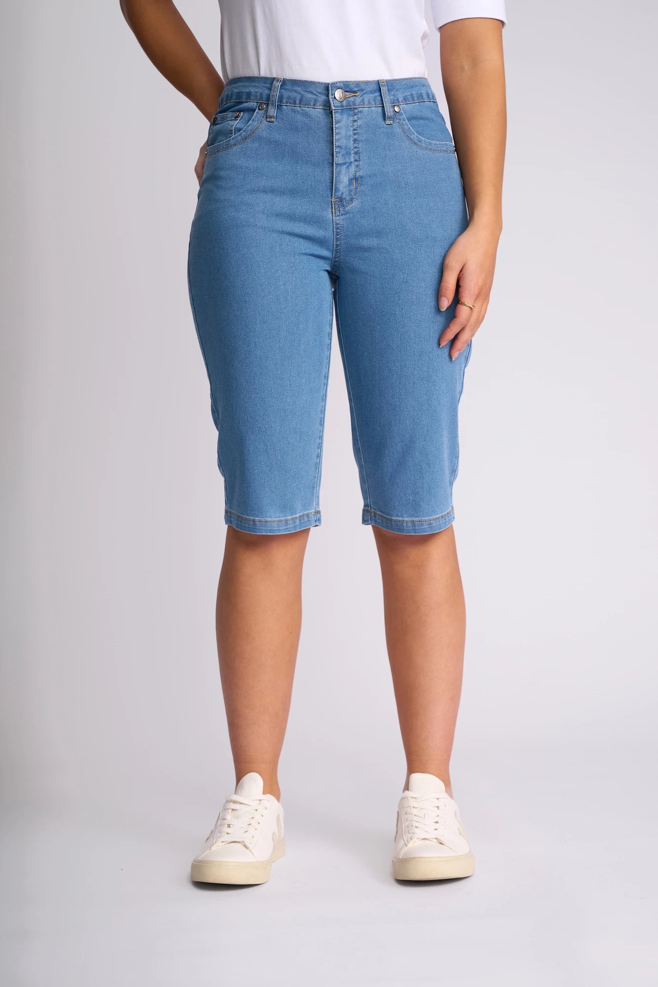 Wearing the Vassalli Alfa Short - Light Denim (Contrast Stitch), these light blue, slim-leg denim shorts are crafted from lightweight stretch denim, making them a true summer staple. Styled here with white sneakers and a white t-shirt against a plain light background.