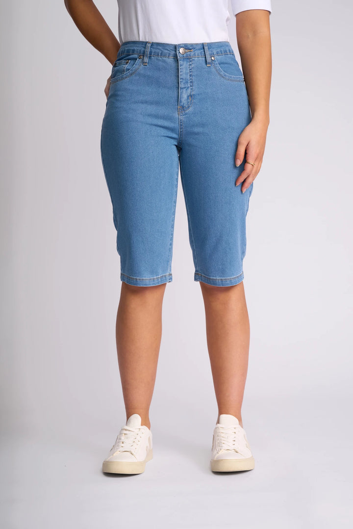 Wearing the Vassalli Alfa Short - Light Denim (Contrast Stitch), these light blue, slim-leg denim shorts are crafted from lightweight stretch denim, making them a true summer staple. Styled here with white sneakers and a white t-shirt against a plain light background.