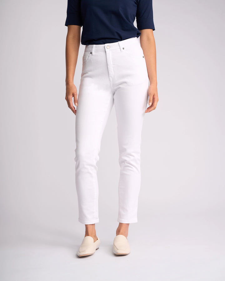 Wearing a navy short-sleeve top, Vassalli's Tide Jean in White Denim, and cream slip-on shoes, the headless individual poses against a plain light background.