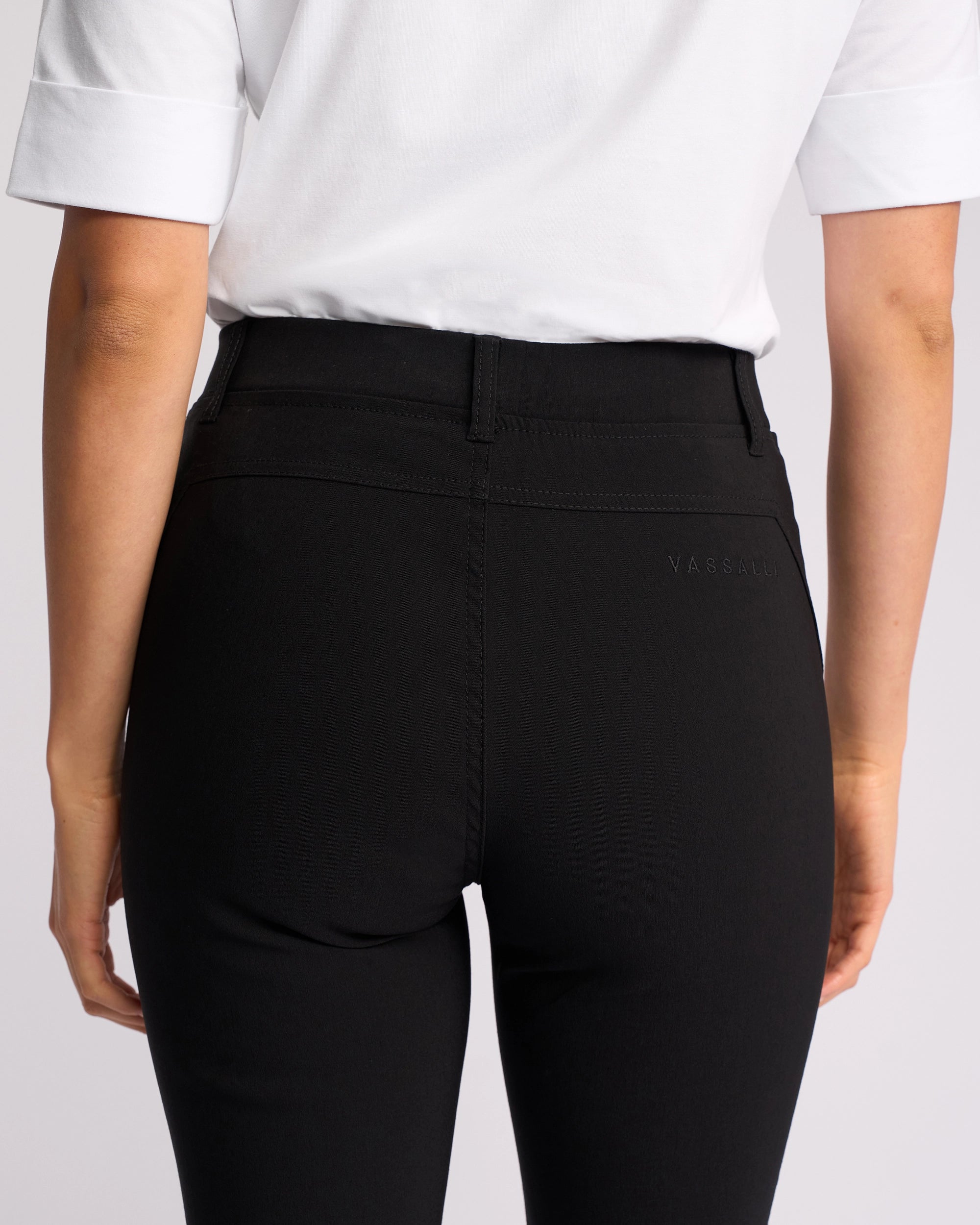 A person is shown from the back wearing Vassalli’s Concept Pant in black, paired with a white short-sleeve shirt, highlighting the waist and upper legs.
