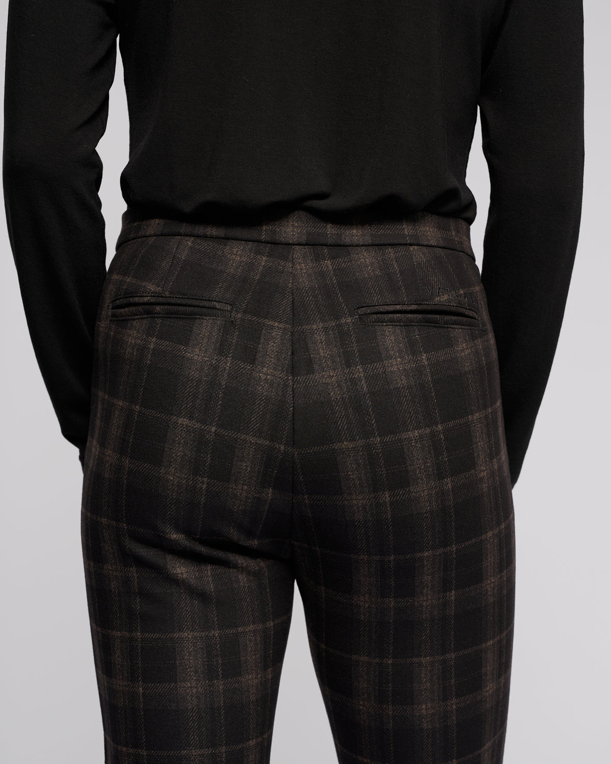 A person is shown from the back wearing a black long-sleeve top and Vassalli's Style Pant - Checkmate, highlighting the waist, upper legs, and two visible back welt pockets on the printed skinny-leg pants.
