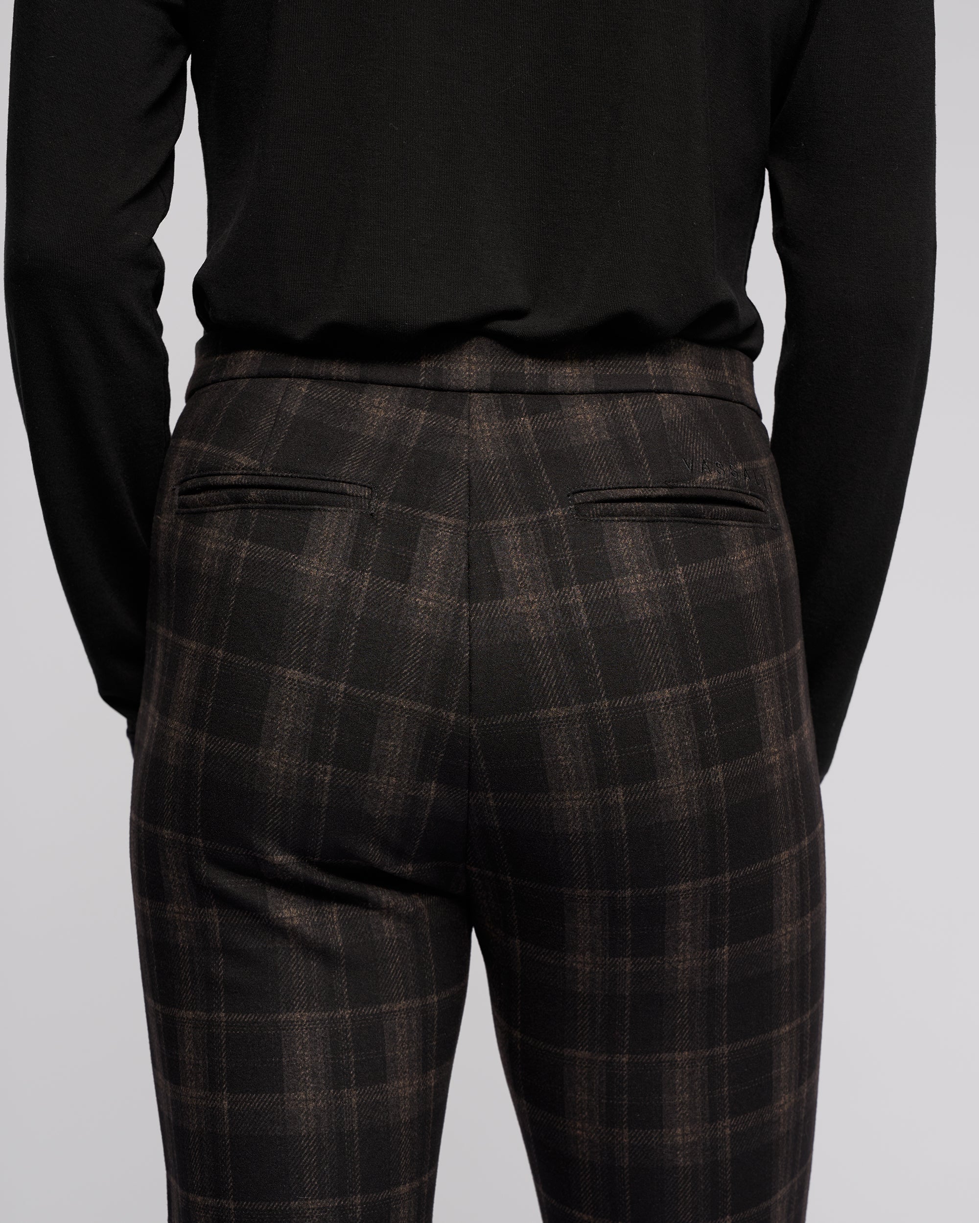 A person is shown from the back wearing a black long-sleeve top and Vassalli's Style Pant - Checkmate, highlighting the waist, upper legs, and two visible back welt pockets on the printed skinny-leg pants.