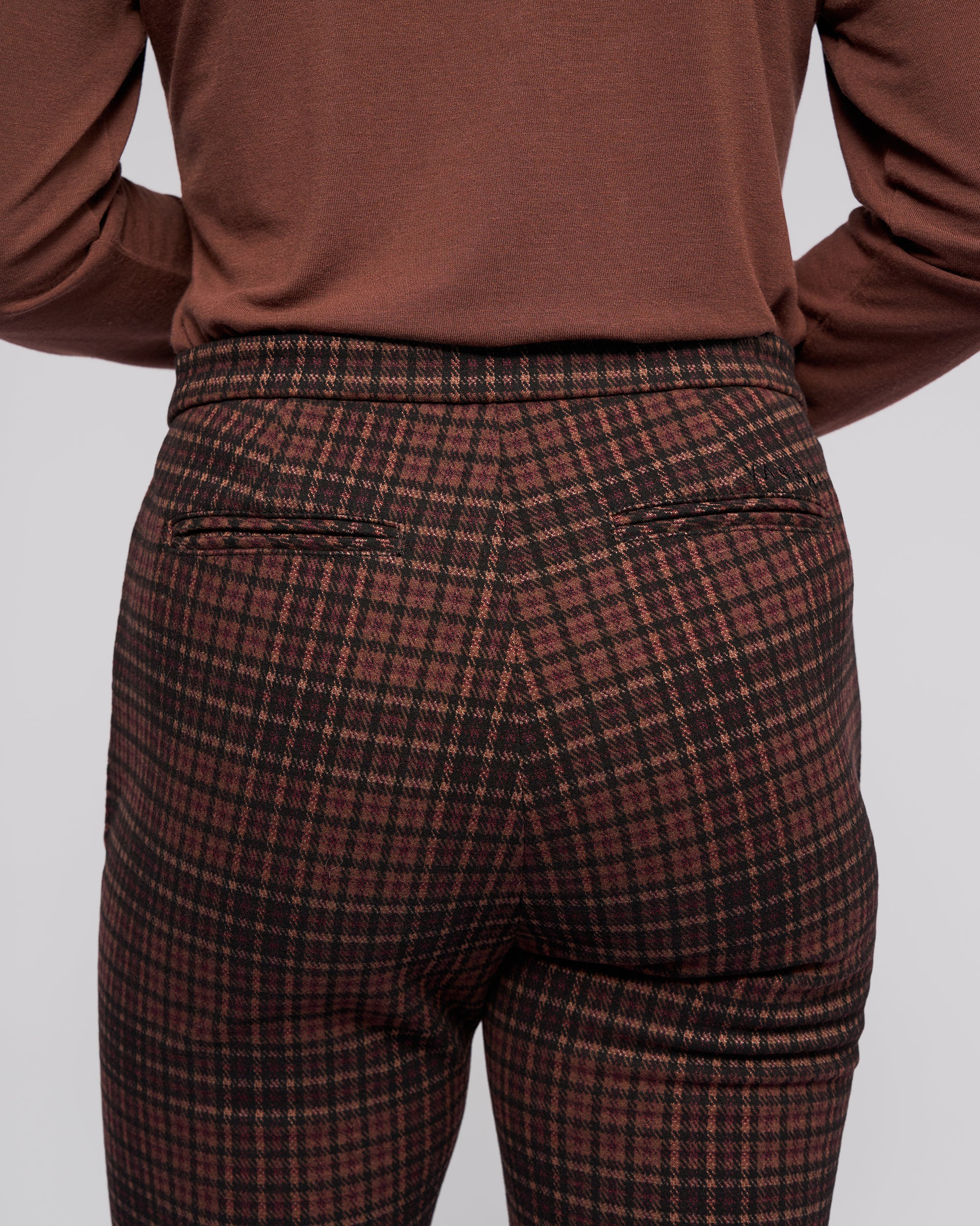 A person is seen from behind wearing Vassalli’s Style Pant - Cherry, featuring a cherry check print, skinny-leg fit, two back pockets, and crafted from stretch knit fabric.