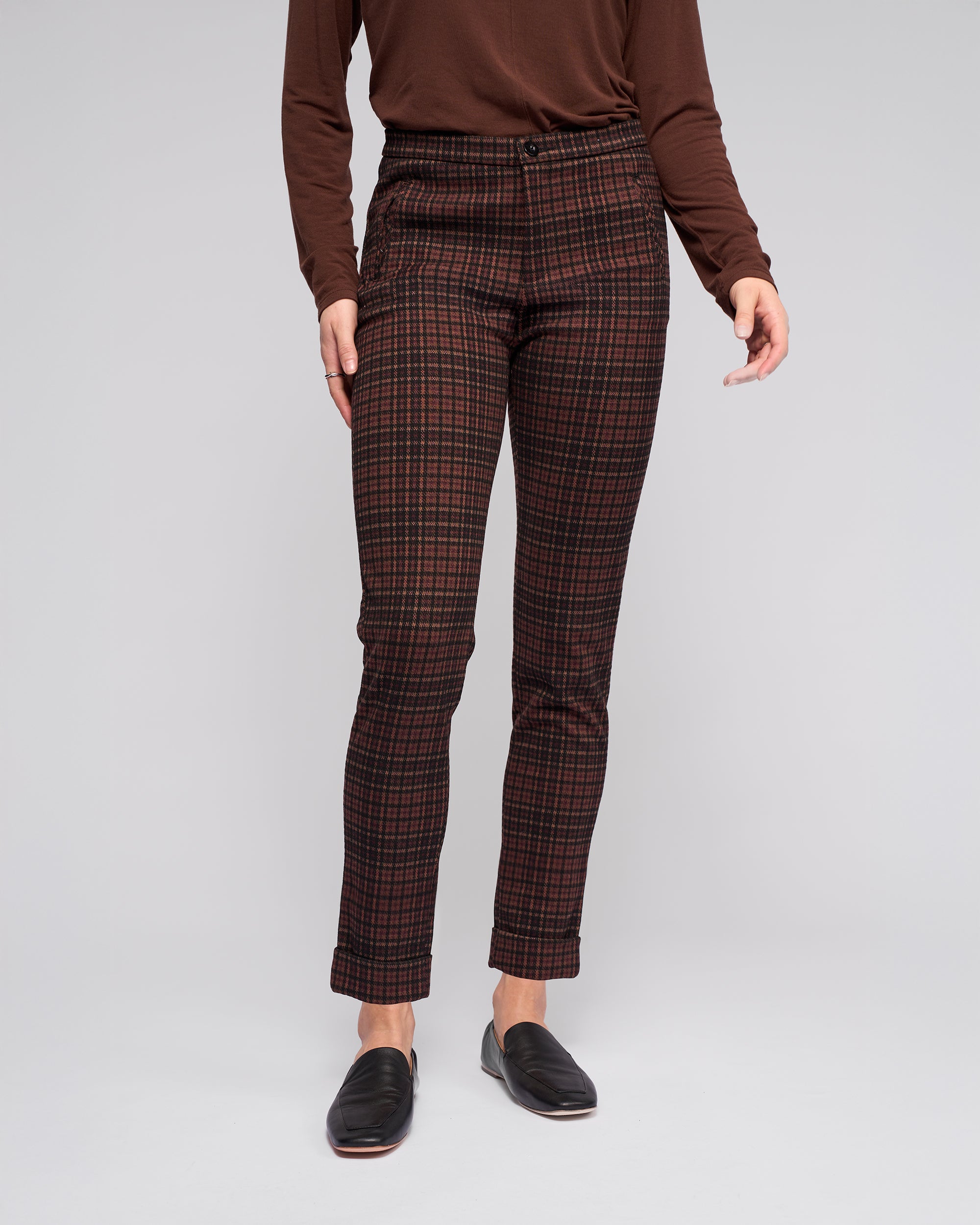 A person wearing a long-sleeve brown top, Vassalli Style Pant - Cherry high-waisted skinny-leg pants, and black loafers stands against a plain light gray background. The image does not show their head.