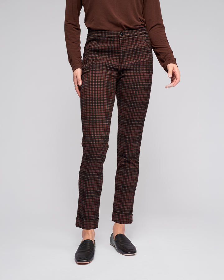 A person wearing a long-sleeve brown top, Vassalli Style Pant - Cherry high-waisted skinny-leg pants, and black loafers stands against a plain light gray background. The image does not show their head.