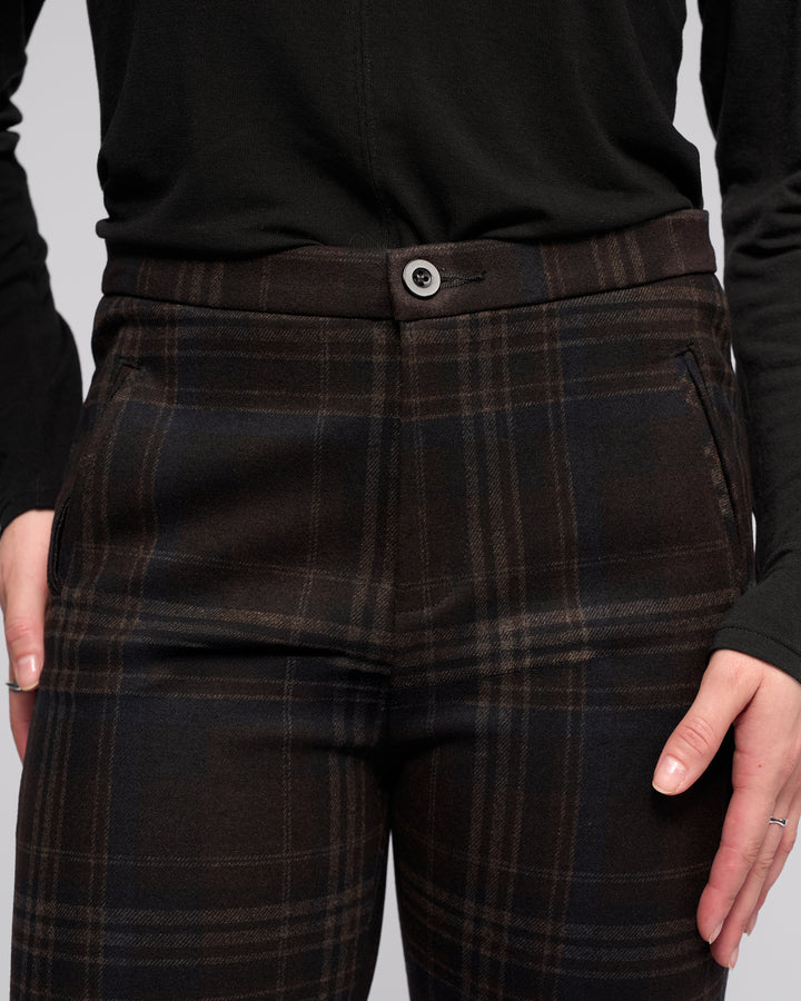 A person wears Vassalli Style Pant - Hugo in dark plaid with a long-sleeve black top, hands by the side pockets. The focus is on the waist and upper legs, excluding the face.