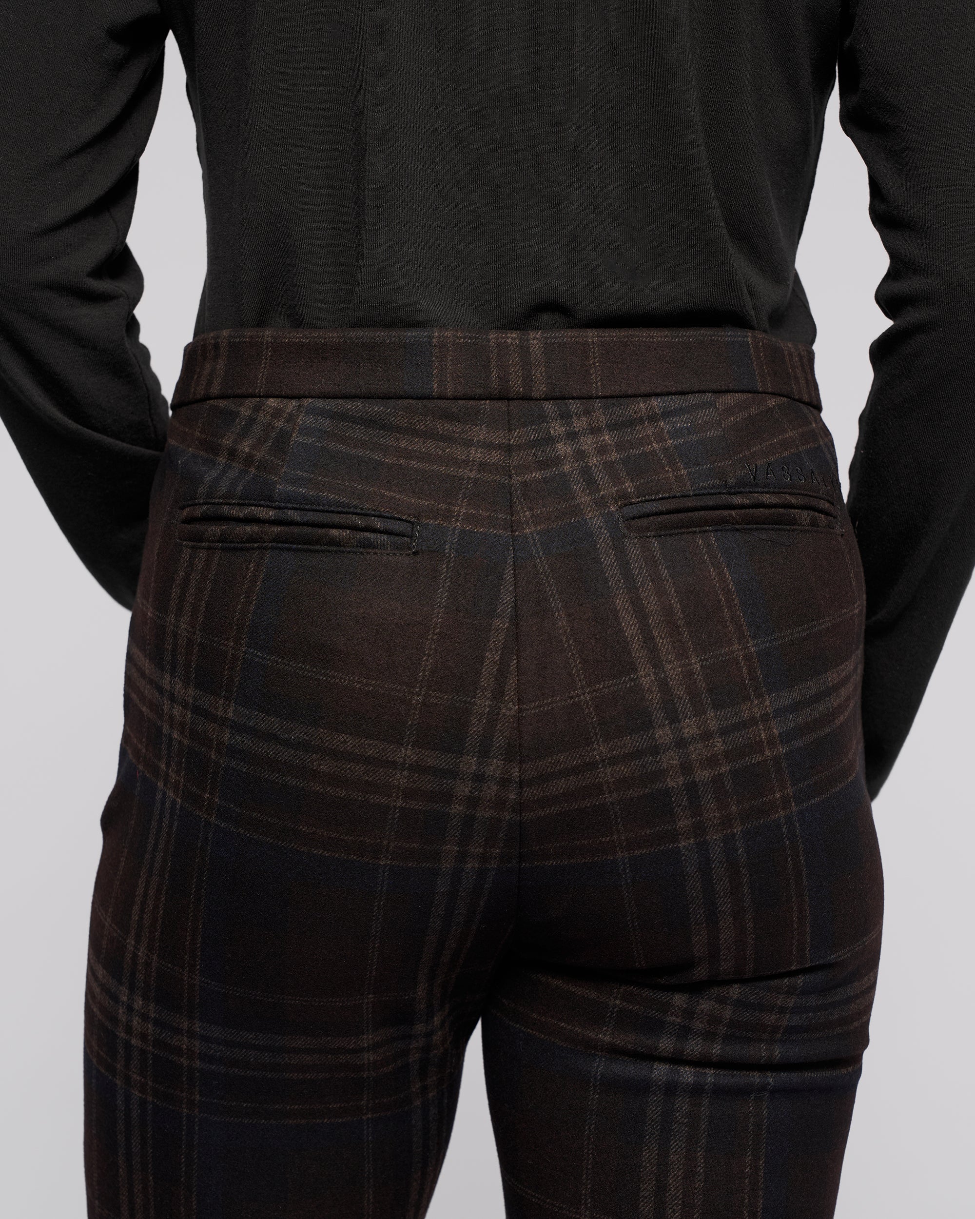 A person is seen from the back wearing Vassalli's Style Pant - Hugo, dark plaid skinny-leg trousers in stretch ponti fabric with two rear welt pockets, paired with a black long-sleeve top.