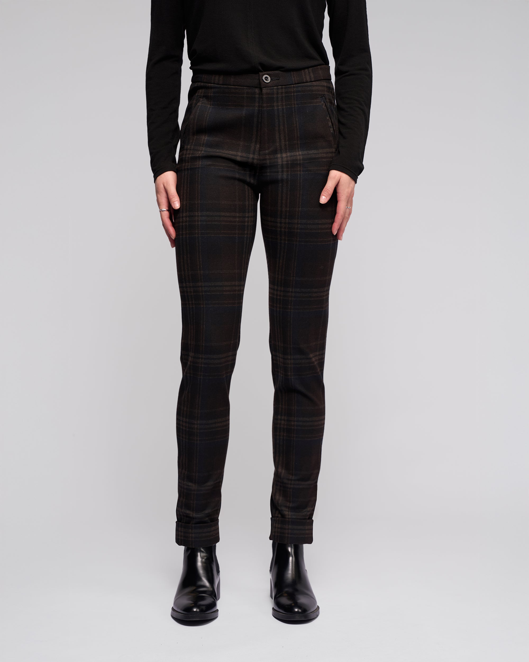 A person, shown from the shoulders down against a plain background, wears a black long-sleeve top, Vassalli Style Pant - Hugo in a check pattern, and black ankle boots.