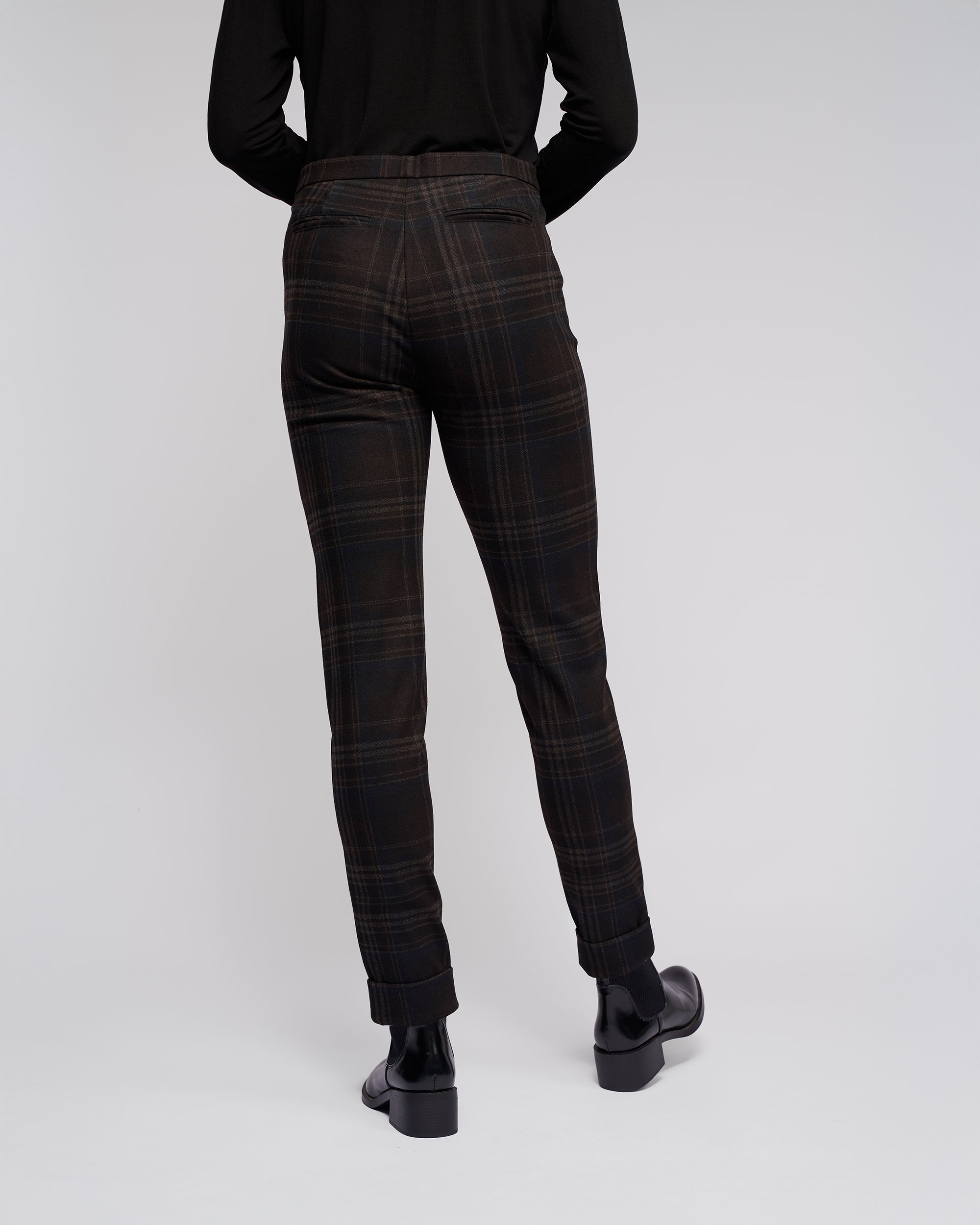Someone wearing Vassalli Style Pant - Hugo, black shoes, and a long-sleeve black top stands with their back to the camera against a plain light background.